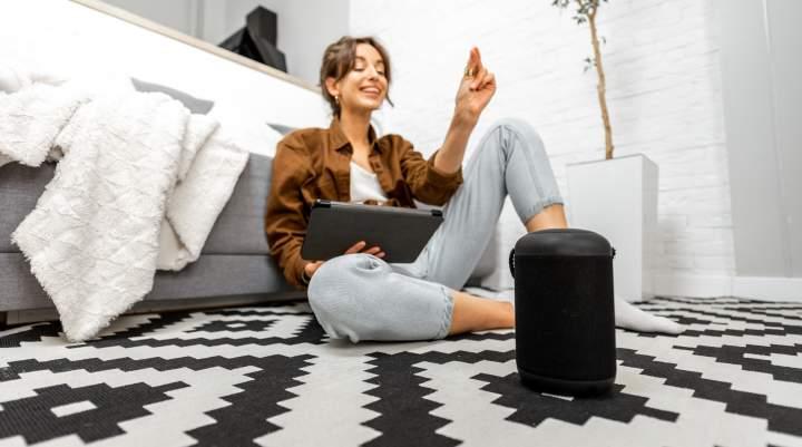 Woman sat on floor in front of sofa engaging with her smart speaker